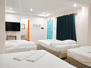 A hotel room with four single beds, a television, a bathroom with a mirror, and a blue door.