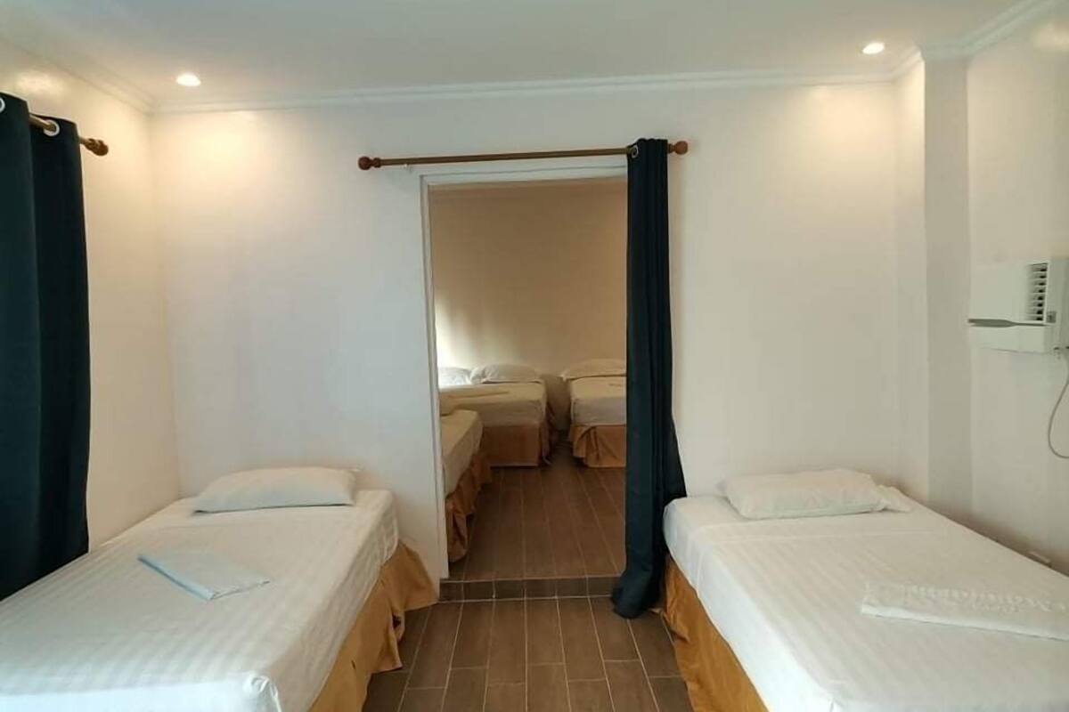 A room with two single beds, a wooden floor, and a curtain on one side.
