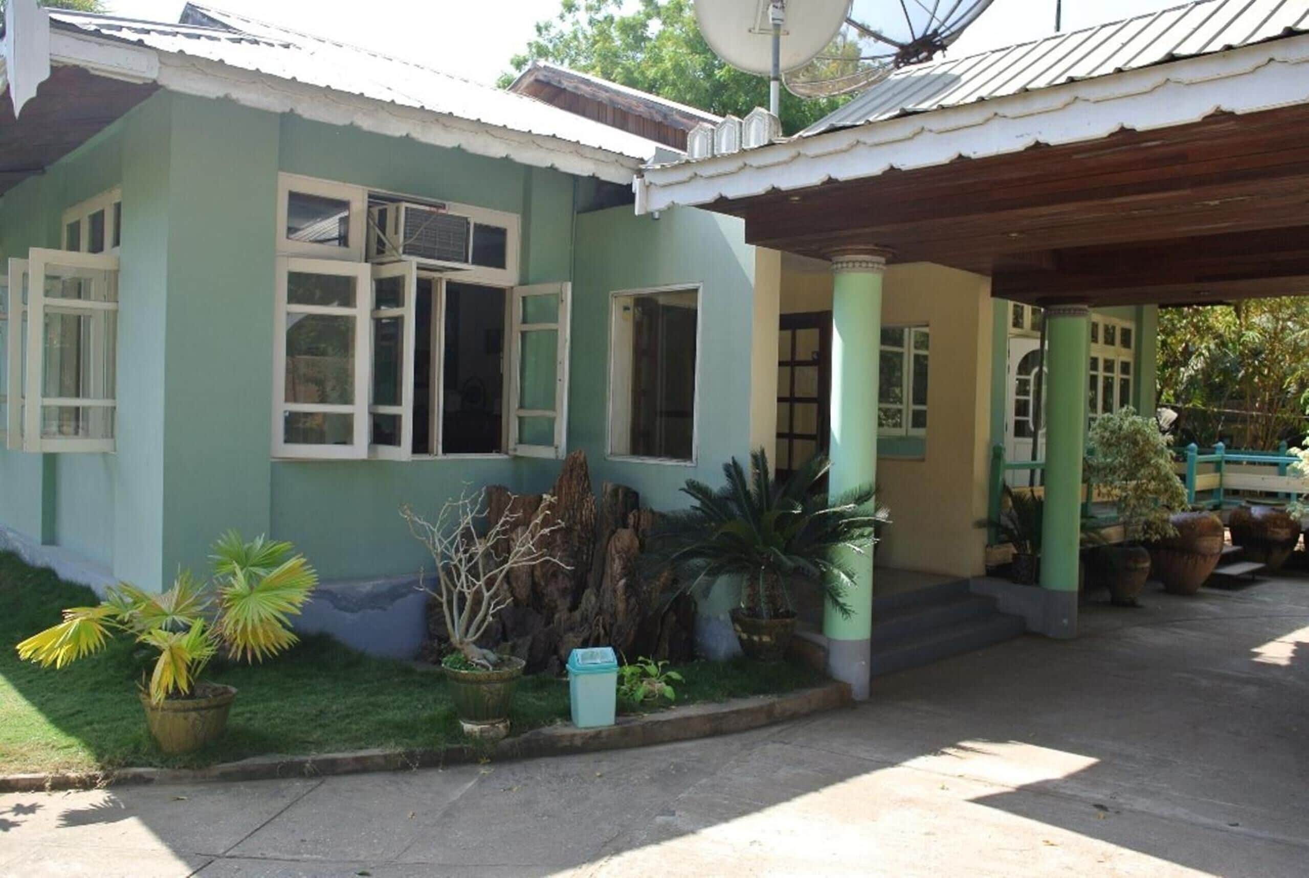 A two-story building with a green facade, multiple windows, and a covered porch area with potted plants.