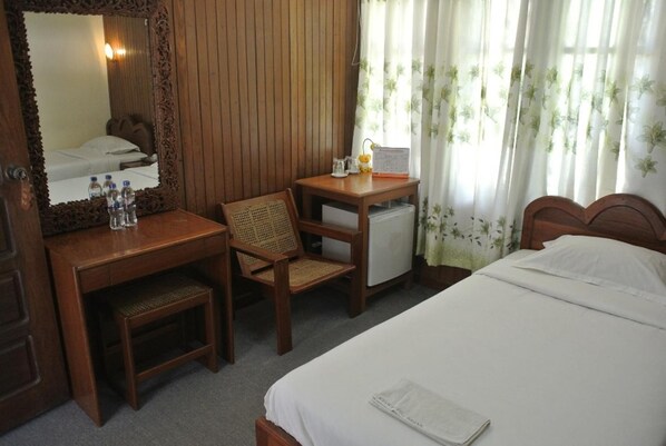 Habitación de hotel con un escritorio de madera, una silla, un refrigerador pequeño, una cama y un espejo.