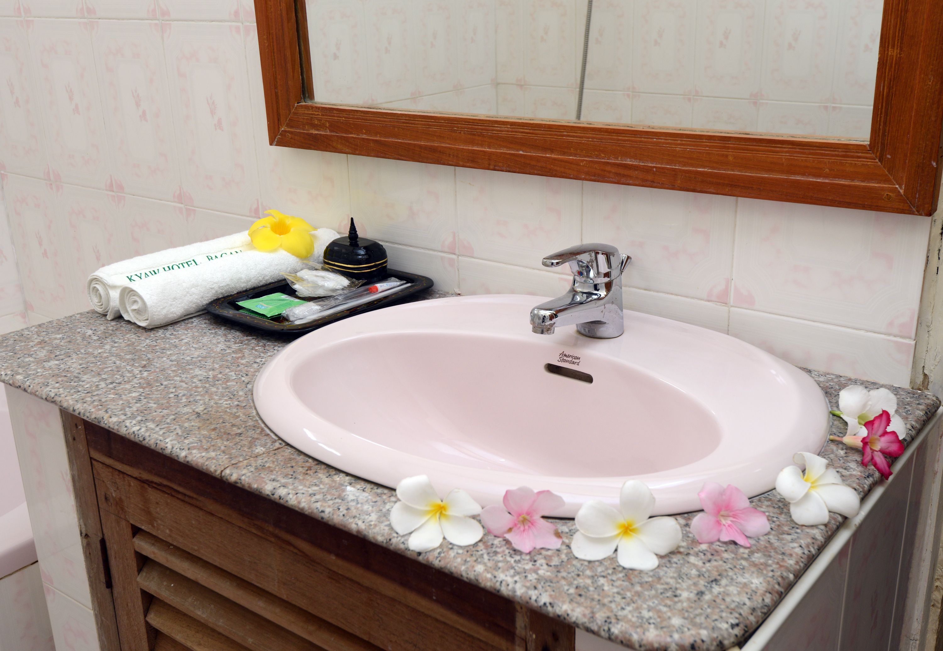 A bathroom sink with a wooden vanity, a mirror above it, and a towel with a hotel name on it.