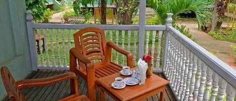 A wooden deck with two chairs and a table, a white balustrade, and lush greenery in the background.