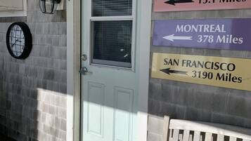 Exterior de un edificio con una puerta azul claro, un banco y señales que indican las distancias a varias ciudades.