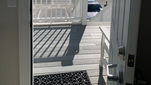 A view from a door to a beachside parking area with a white fence and a white car parked. - The Ocean View (Centerville)