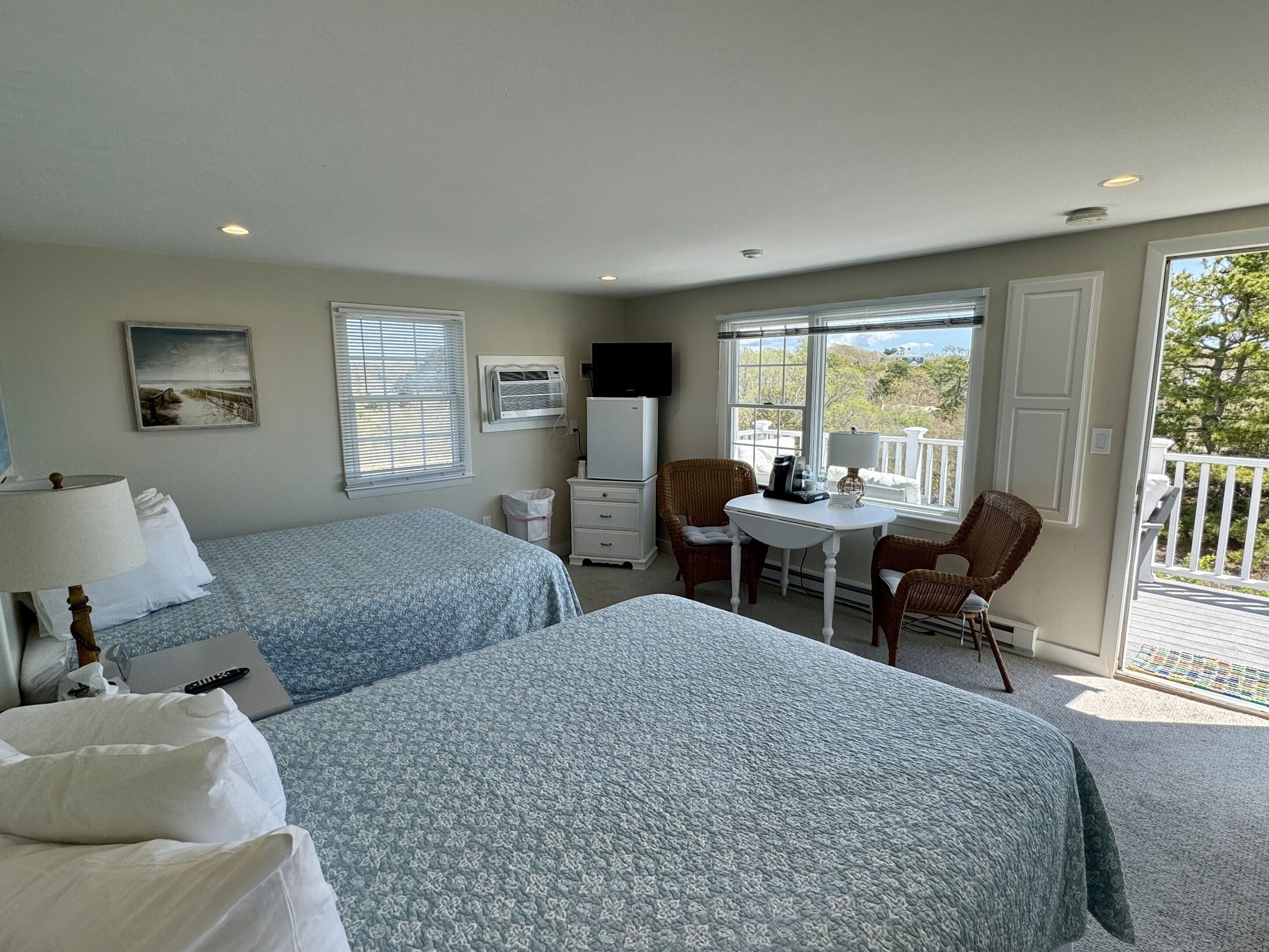 A bedroom with two beds, a desk, a chair, a TV, and a window with a view.