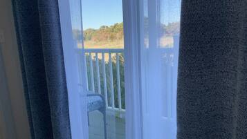 A view through a screened door to a balcony with a white railing and a chair.