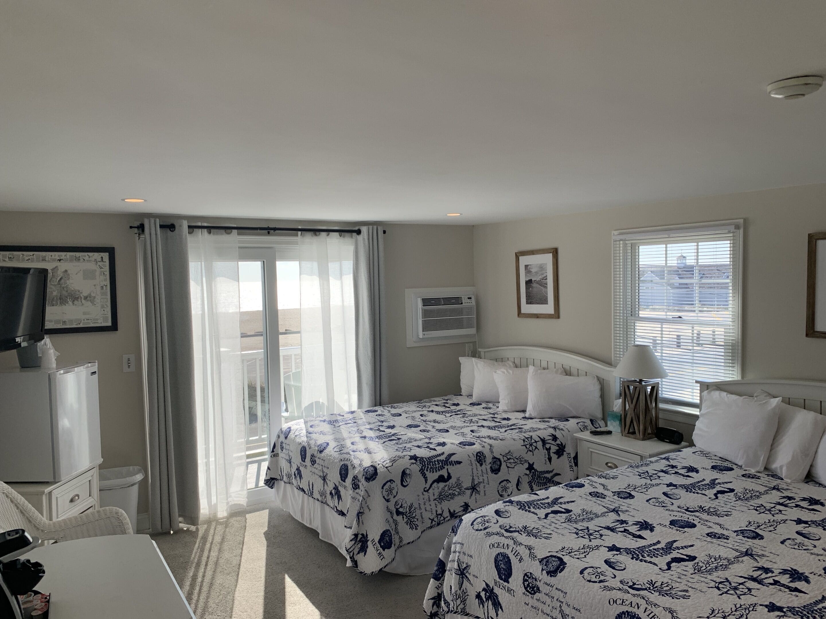 A hotel room with two beds, a TV, a desk, and a balcony with curtains.