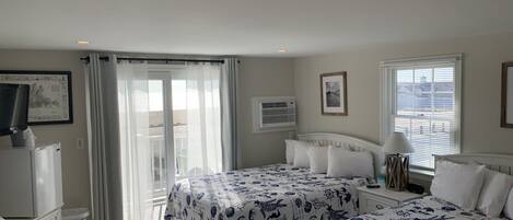 A hotel room with two beds, a TV, a desk, and a balcony with curtains.