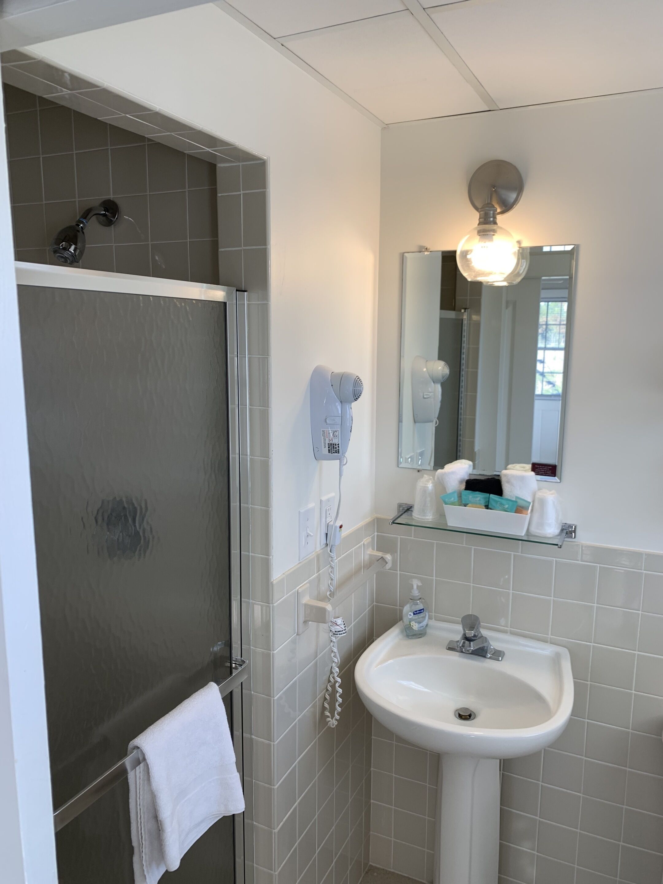 Un baño con ducha, lavamanos, secador de pelo y espejo con luz.