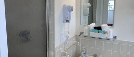 Un baño con ducha, lavamanos, secador de pelo y espejo con luz.