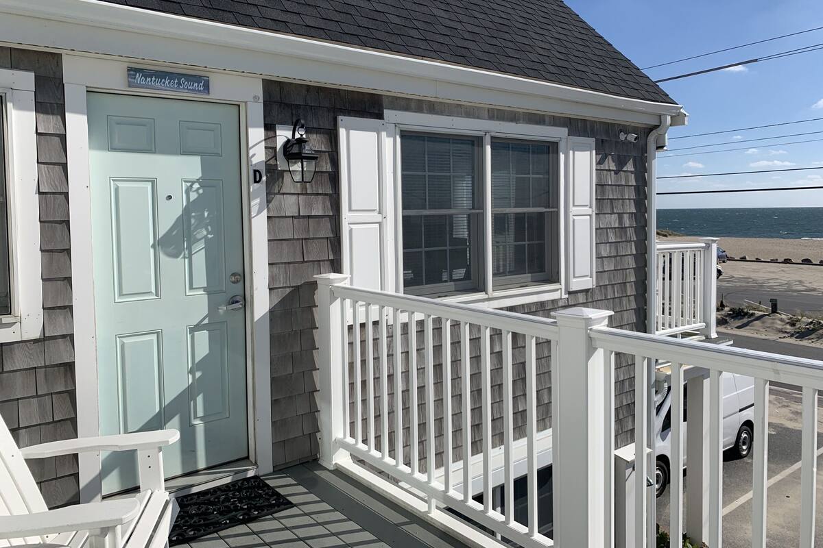 A coastal house with a light blue door, white railings, and a view of the beach.