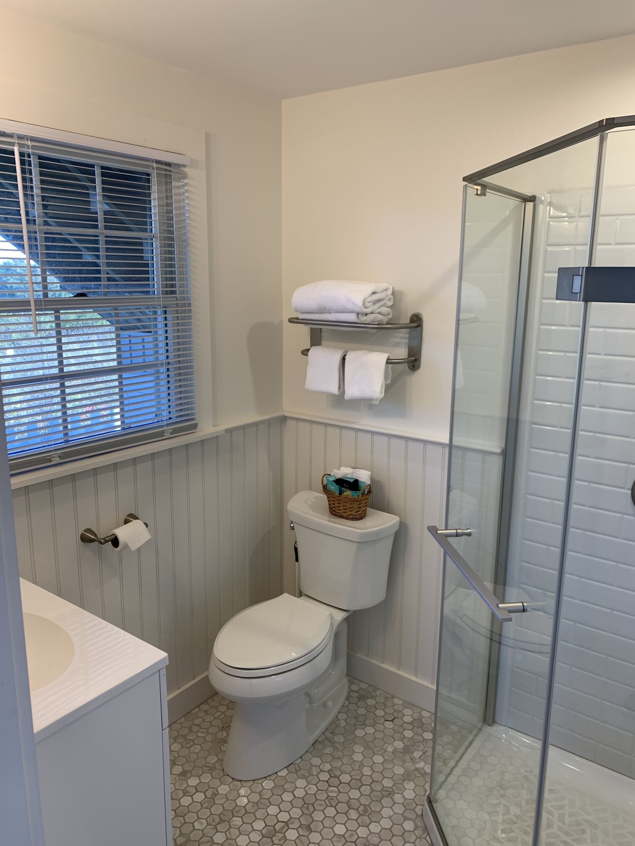 Un baño con inodoro, ducha y ventana con persianas.