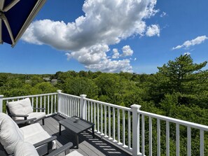 Um terraço com móveis de exterior, guarda-corpo branco e vista para uma paisagem arborizada.