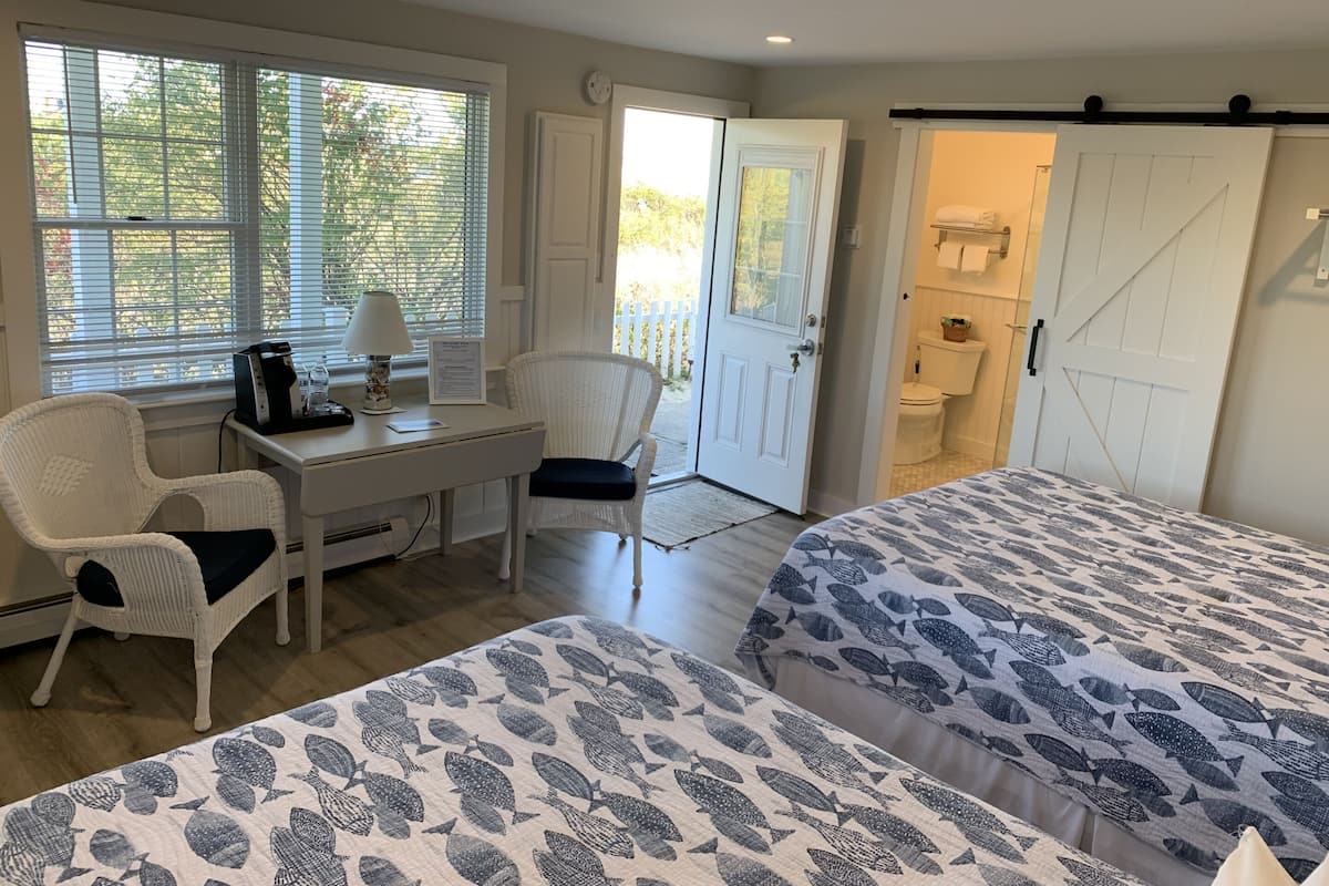 A room with two beds, a desk, a chair, and a door leading to a bathroom.