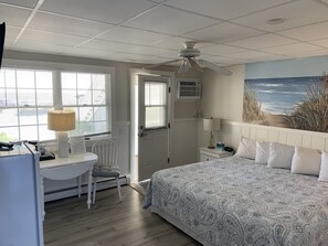 Une chambre à coucher comprenant un lit, un bureau, une chaise, un ventilateur de plafond et une fenêtre avec des stores.
