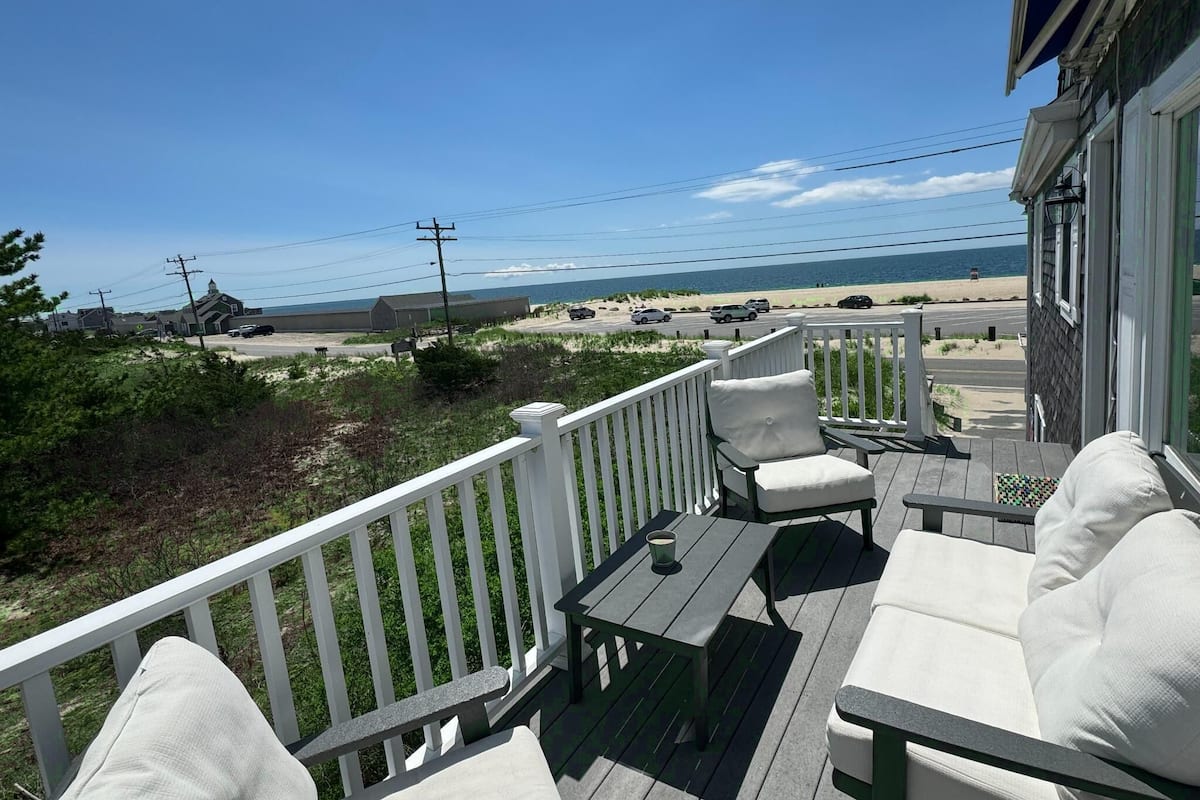 A deck with outdoor furniture, a view of the beach, and a building in the background.