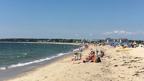 A beach with people sunbathing and swimming, and beach chairs and umbrellas. - The Ocean View (Centerville)