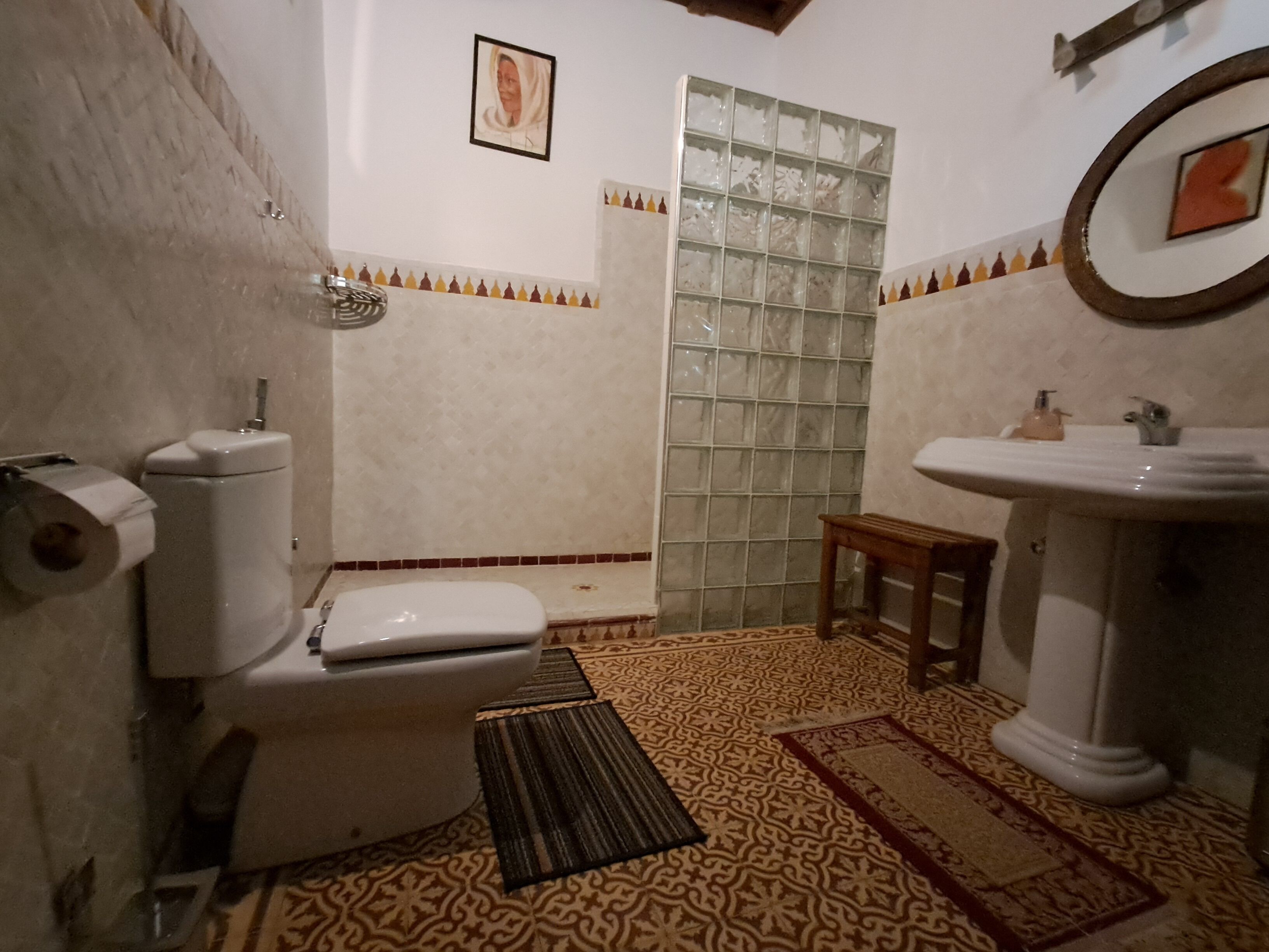 Un baño con inodoro, lavabo, ducha, suelo estampado y un cuadro en la pared.
