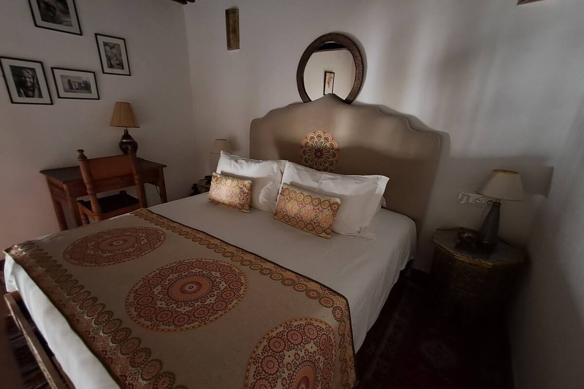 Une chambre à coucher avec un lit, une chaise, une table de chevet et un miroir au mur.