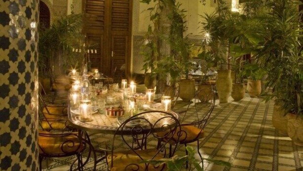 An indoor dining area with a round table, chairs, candles, and potted plants. - Riad Al Bartal (Fes)