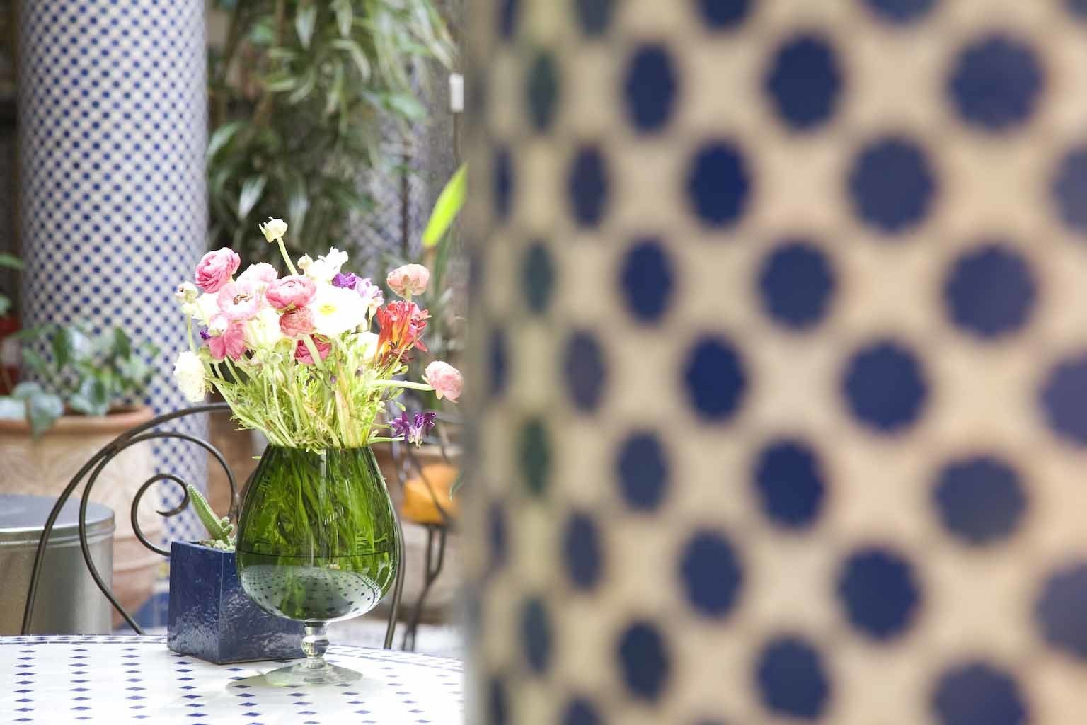 Uma mesa com um vaso verde contendo flores rosa e brancas, sobre uma mesa com padrão azul e branco.