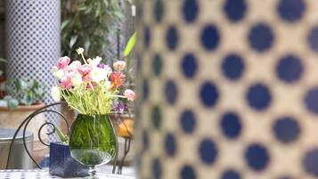 Uma mesa com um vaso verde contendo flores rosa e brancas, sobre uma mesa com padrão azul e branco.