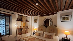 A cozy bedroom with a wooden ceiling, a large bed with patterned bedding, a stone wall, and a small table with a lamp. - Riad Al Bartal (Fes)