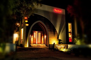 Un edifici amb un arc d'entrada destacat, un cartell que diu "Bagan Nov" i una banca a l'exterior.