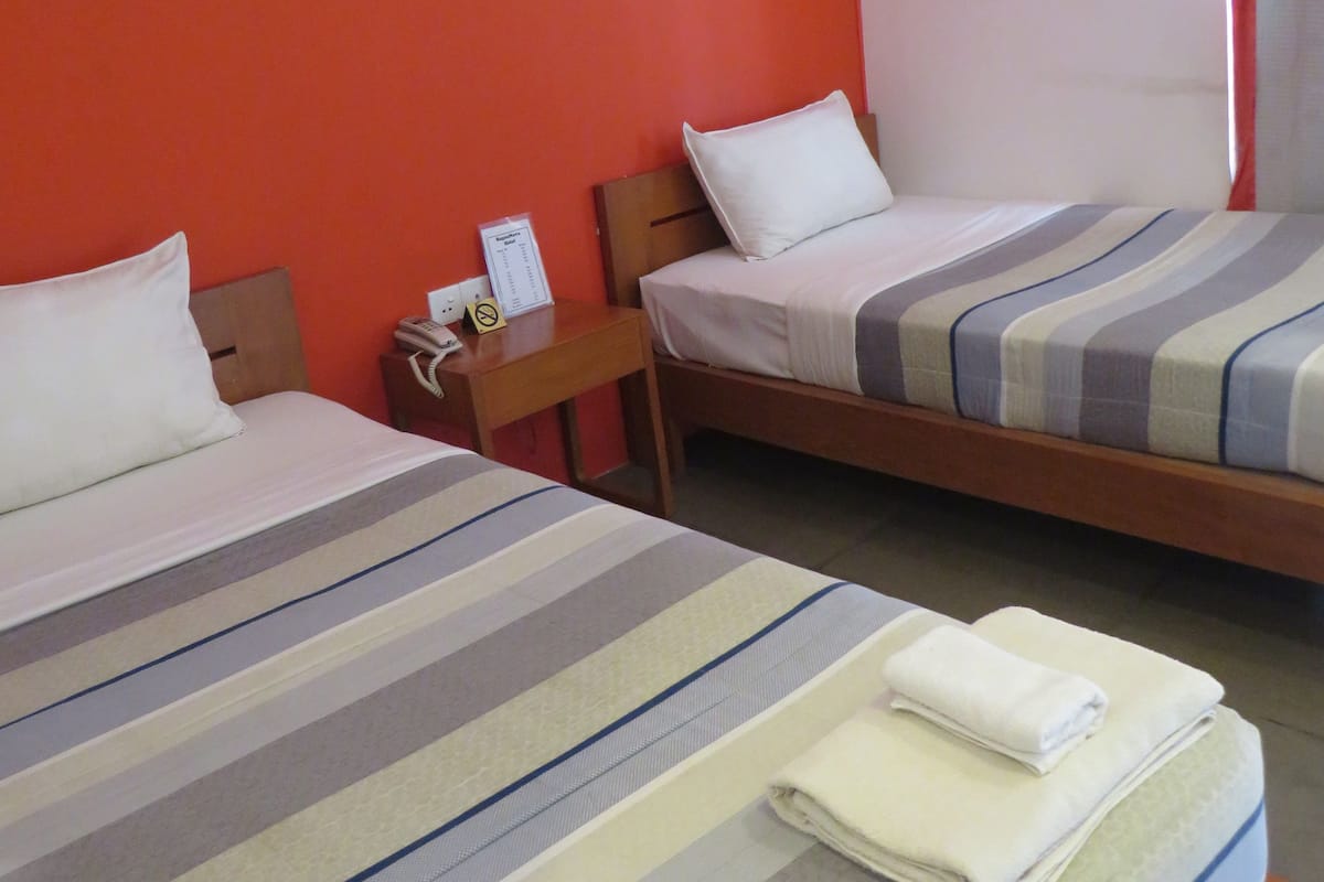 Habitación de hotel con dos camas, una mesita de noche de madera, un teléfono y una ventana con cortina.
