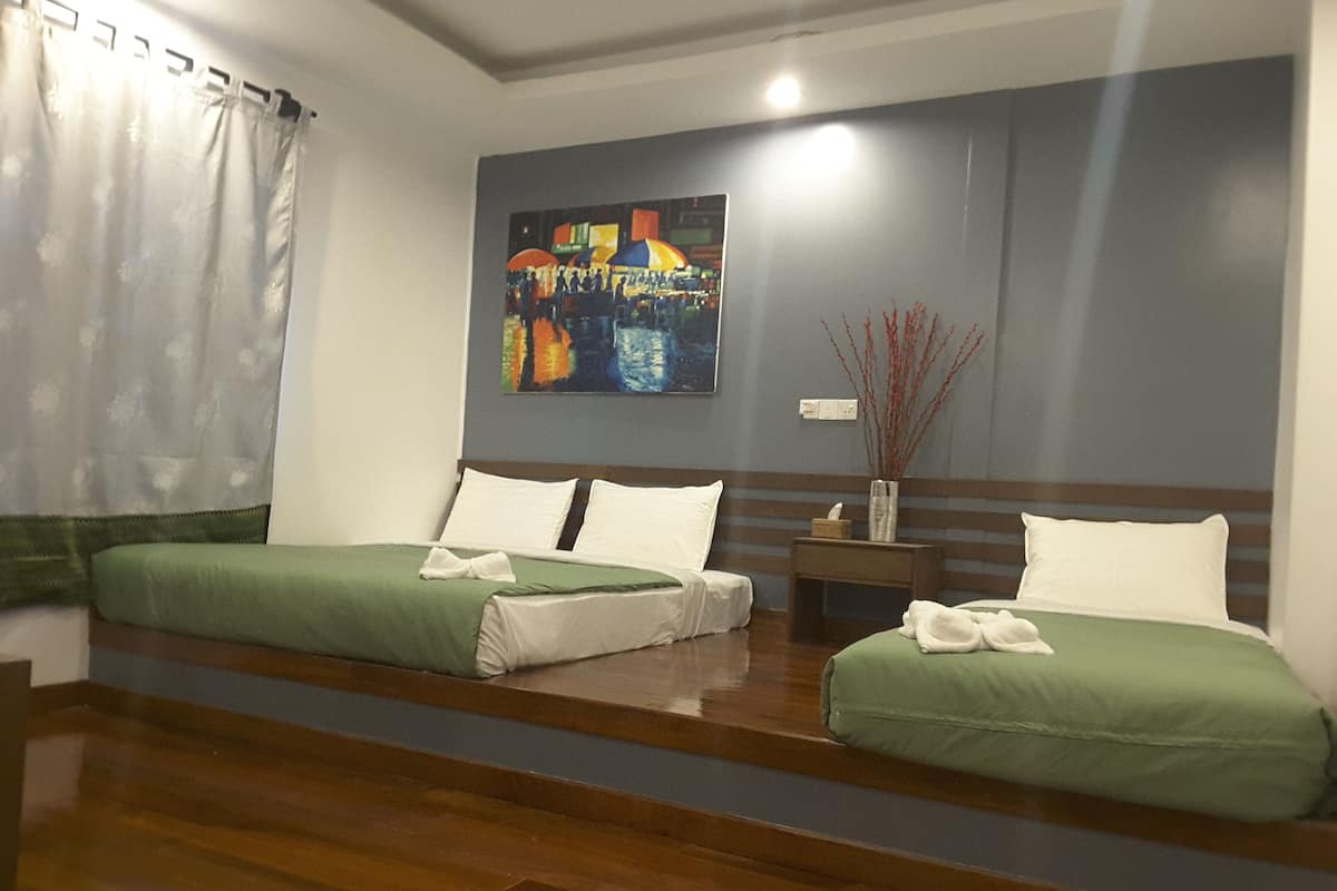 Una habitación de hotel con dos camas individuales, piso de madera, un cuadro en la pared y una mesita de noche con un florero.