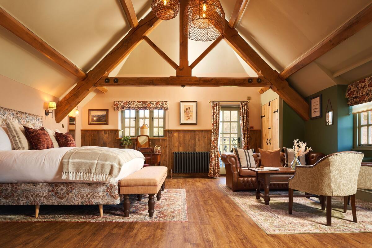 A spacious bedroom with a large bed, a wooden ceiling, and a cozy seating area with a table and chairs.
