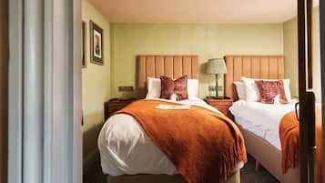 Quarto de hotel com duas camas, uma mesa de cabeceira com abajur e uma tomada na parede.
