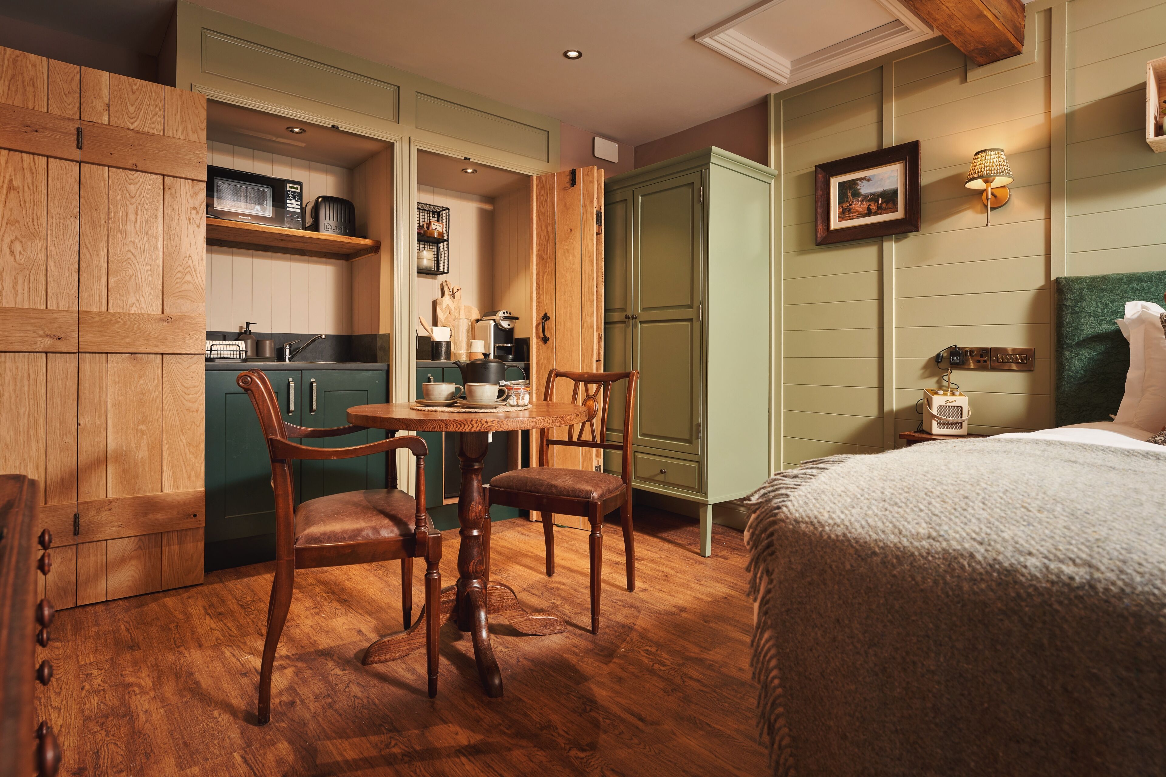 A compact room with a bed, a dining table with chairs, a kitchenette, and a wardrobe.