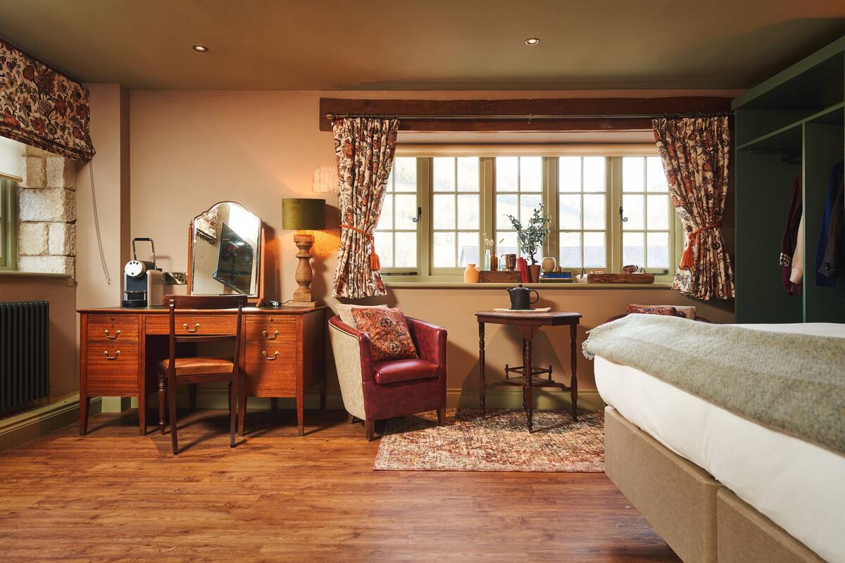 A bedroom with a wooden dresser, a red armchair, a bed, a window with curtains, and a radiator.