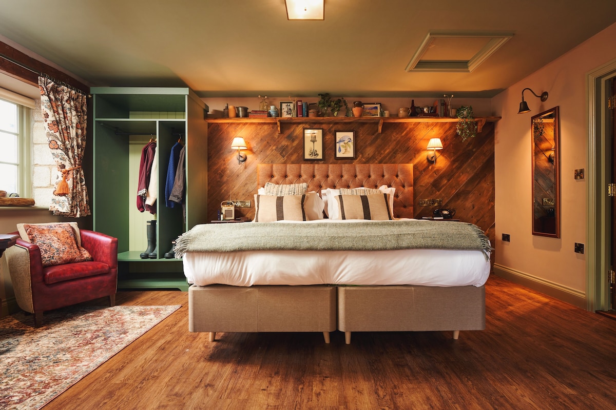 Un dormitorio con una cama grande, un sillón rojo, piso de madera y pared verde.
