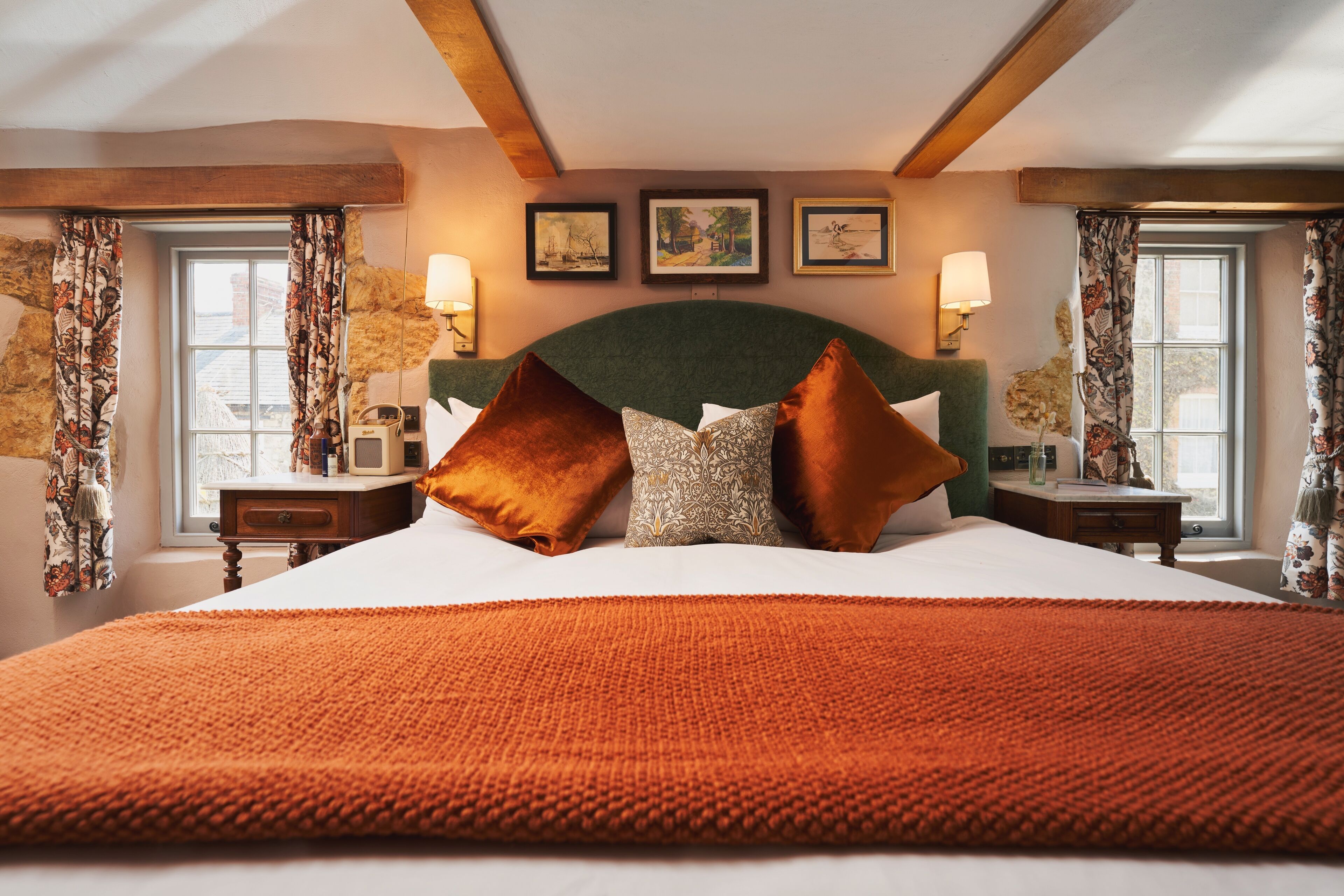 A large bed with a green headboard, multiple pillows, and a red blanket. There are two bedside tables with lamps and framed pictures on the wall above the bed.