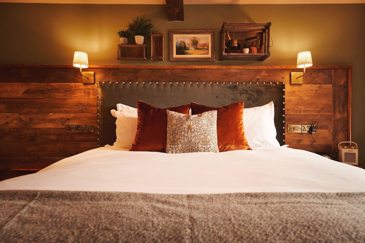 A bed with a wooden headboard, two wall-mounted lamps, and a framed picture above.