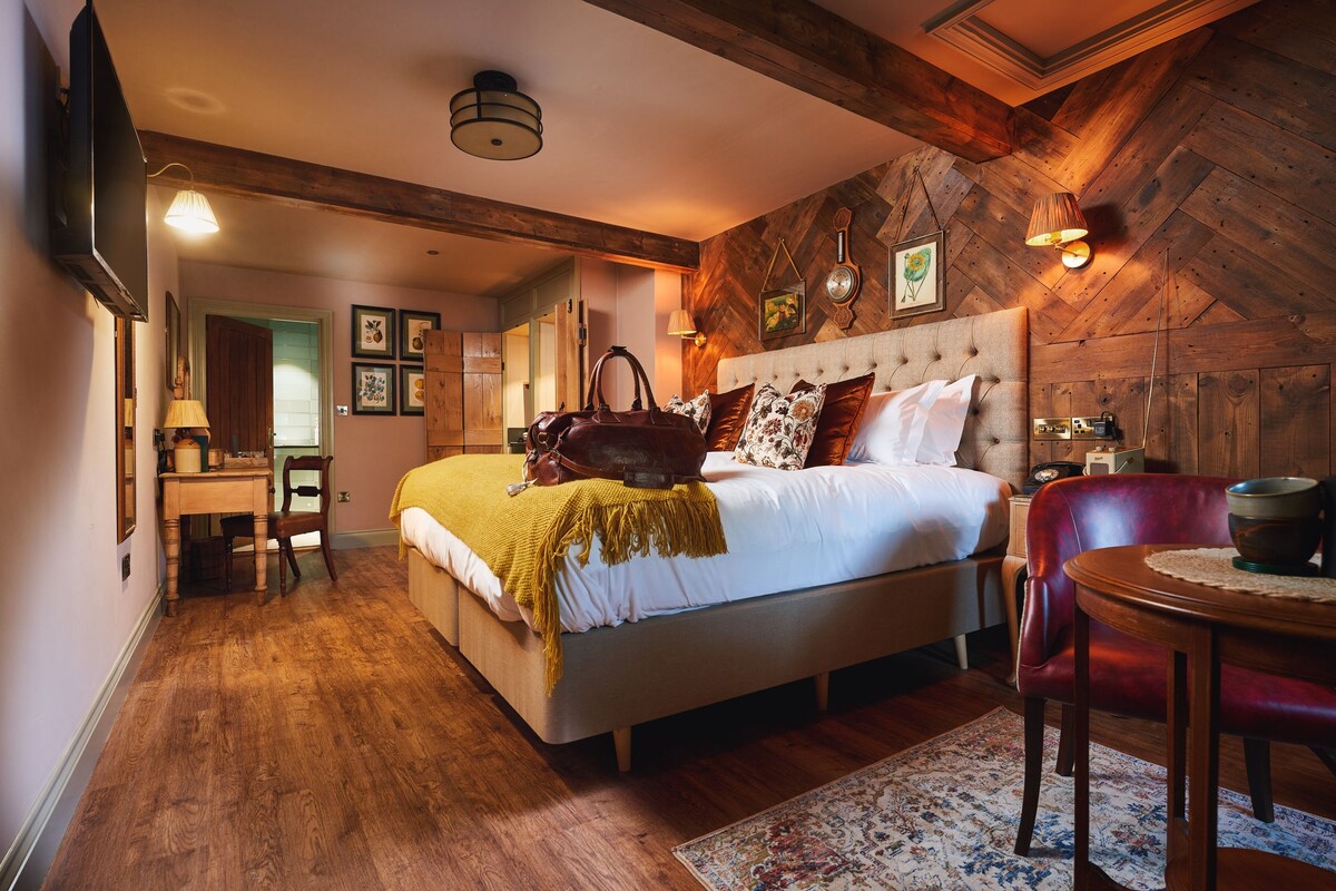 A bedroom with a wooden ceiling, a bed with a headboard, a desk, and a chair.