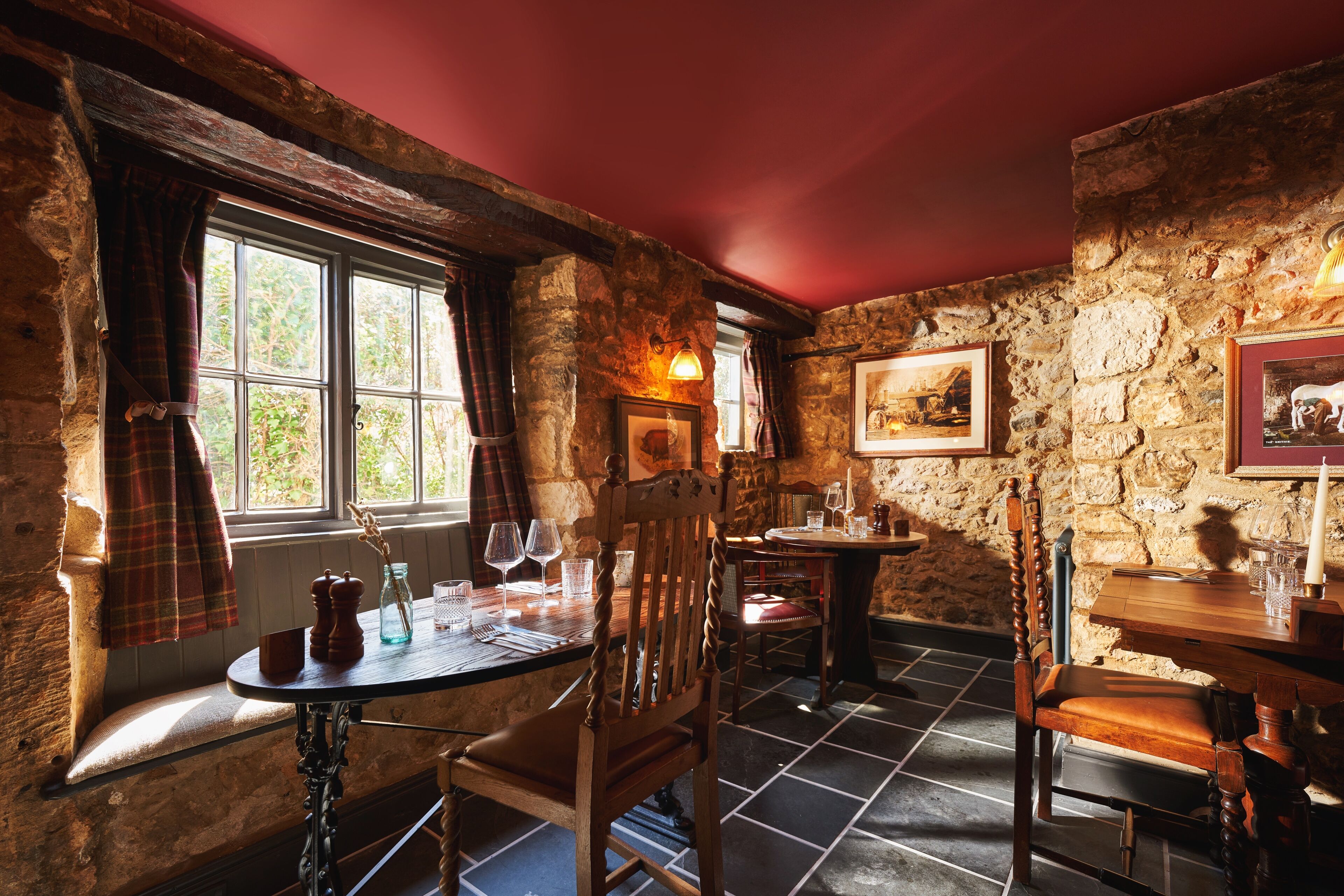 A rustic interior with stone walls, wooden furniture, and a window with plaid curtains.