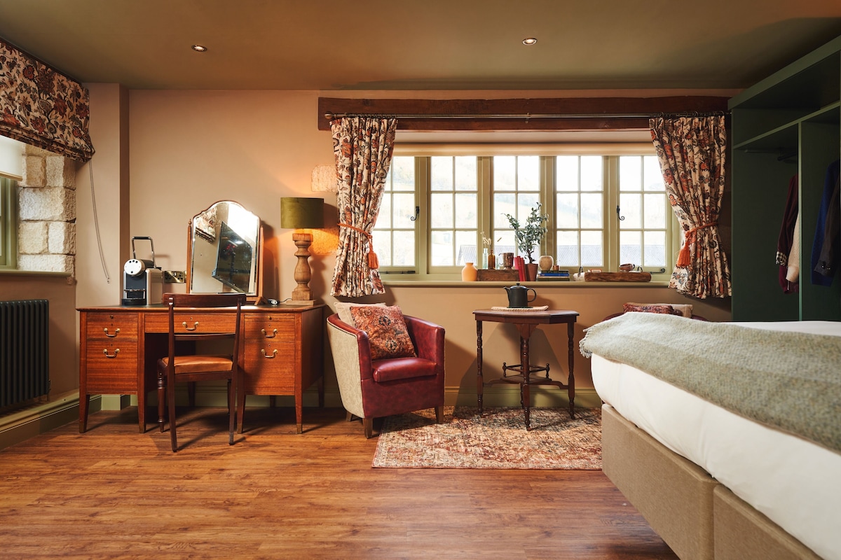 Un dormitorio con cómoda de madera, un sillón rojo, una cama, una ventana con cortinas y un radiador.