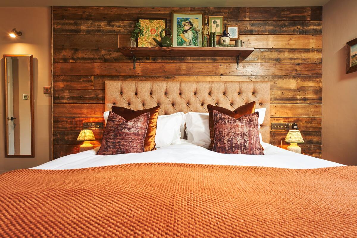 A bedroom with a wooden headboard, a large bed with white linens, two decorative pillows, and two bedside lamps.