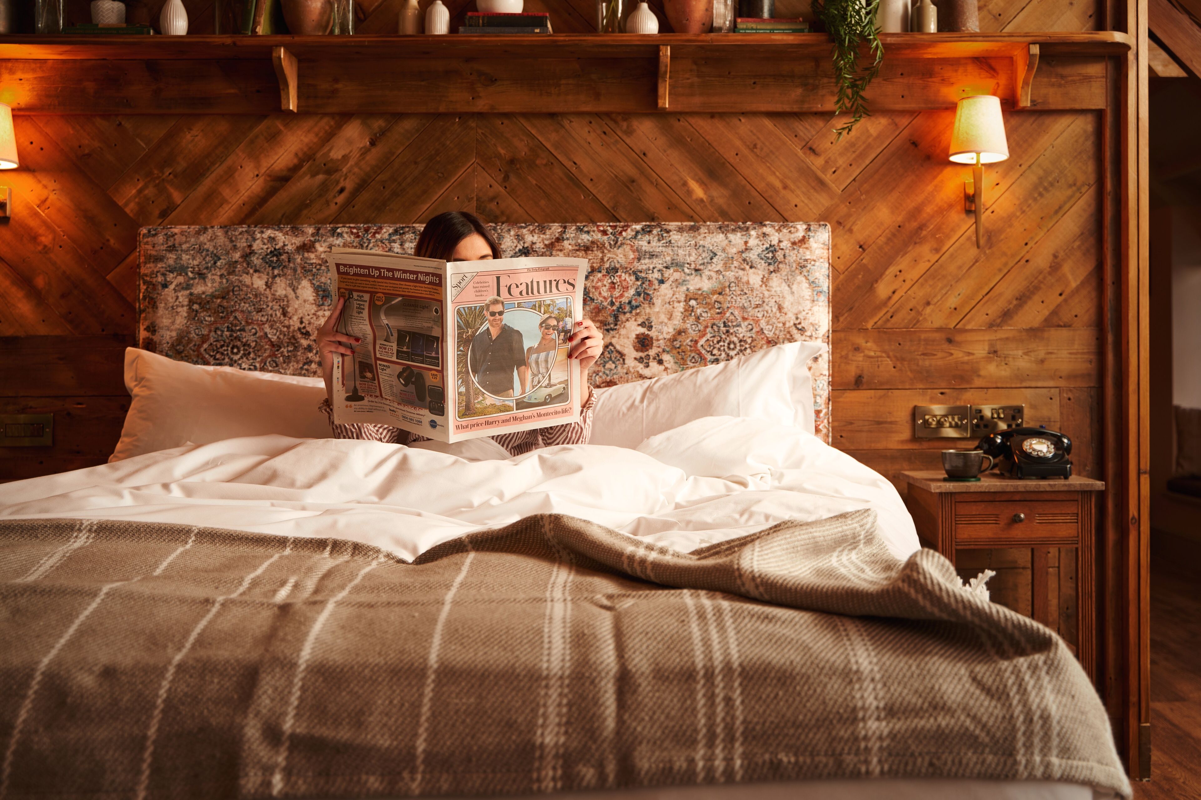 Un lit avec une tête de lit à motifs, une literie blanche et une table de chevet sur laquelle se trouvent une lampe et une radio ancienne.