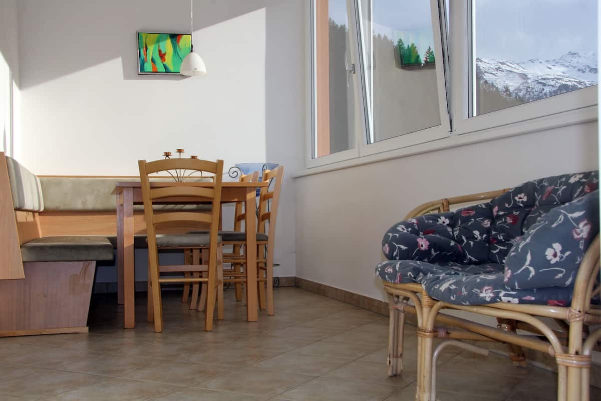 A room with a dining table and chairs, a sofa, a painting on the wall, and a window with a mountain view.