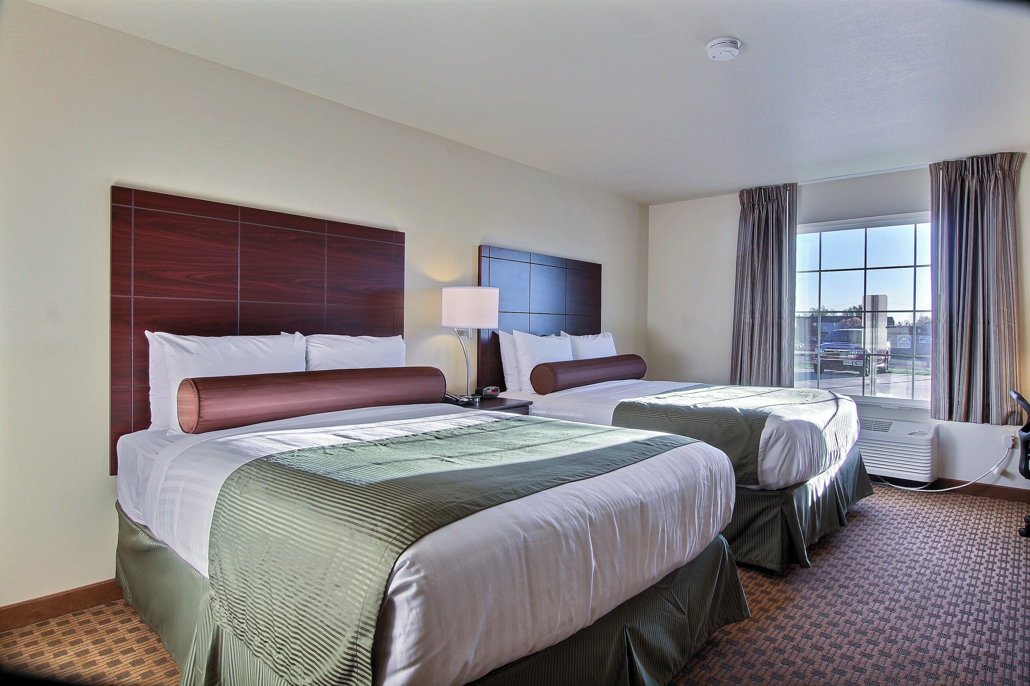A hotel room with two beds, a window with curtains, and a view of the outside.