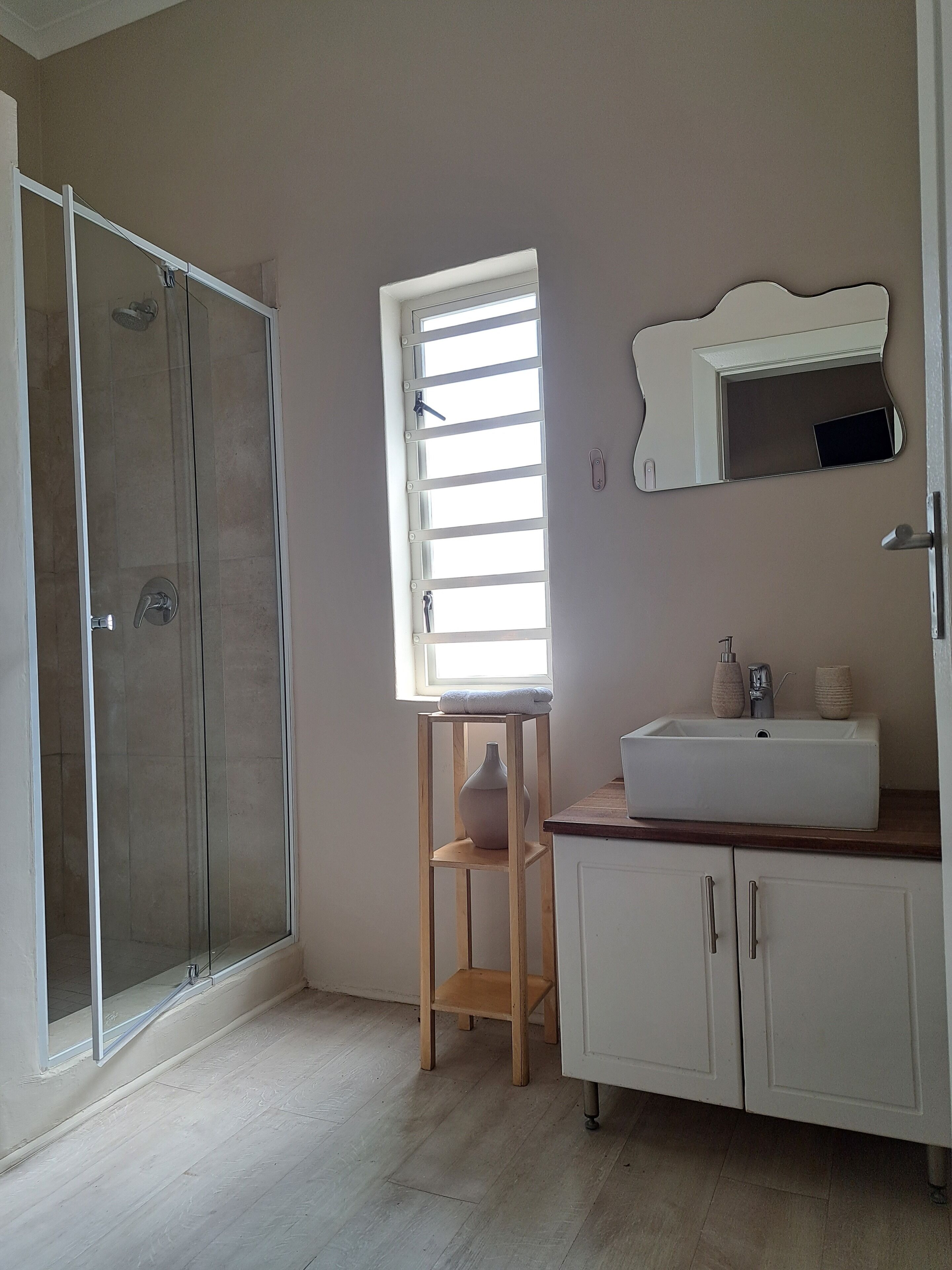 A bathroom with a shower, a window, a sink, and a mirror.