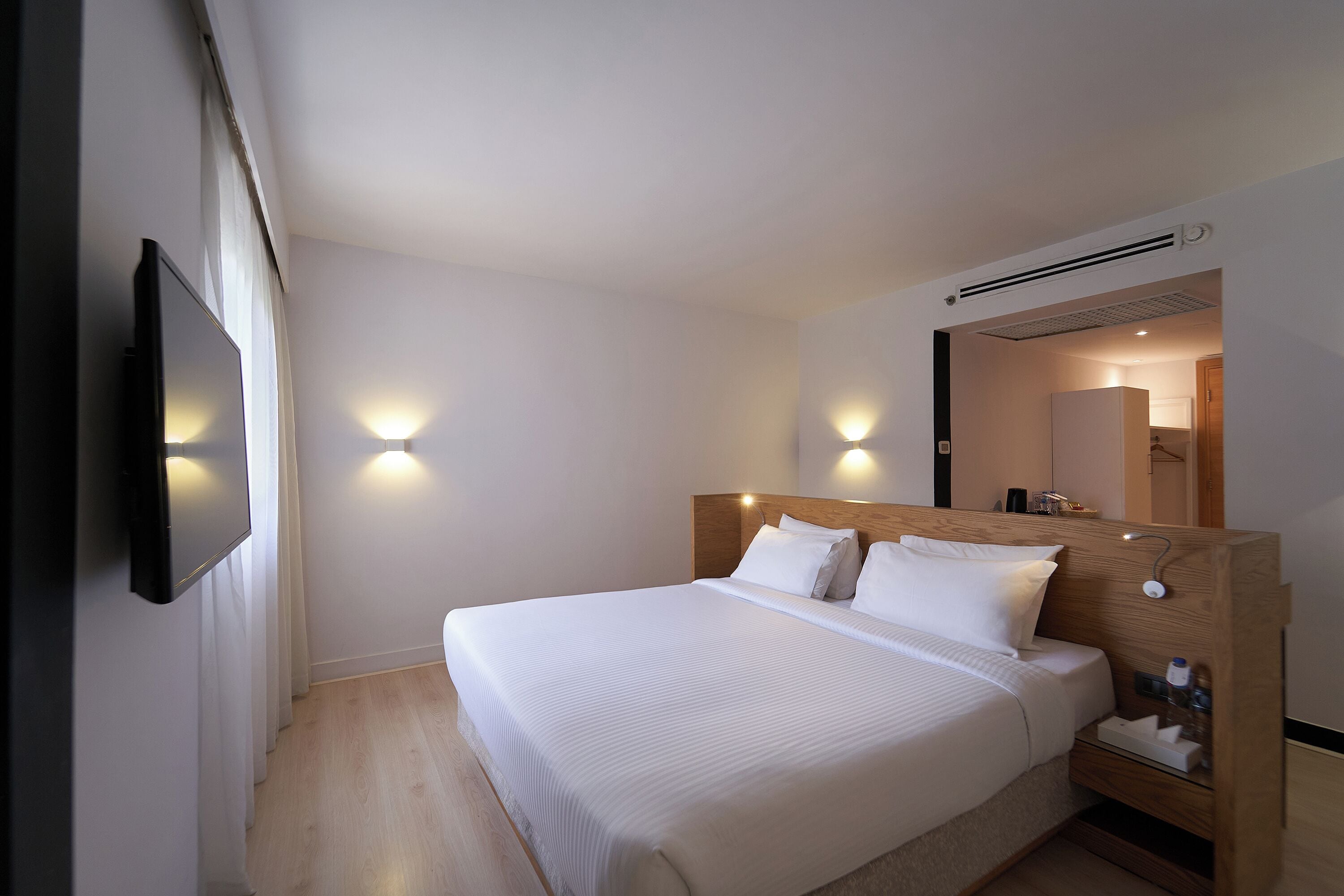 Habitación de hotel con una cama grande, mesitas de noche, un televisor de pantalla plana montado en la pared y dos lámparas de pared.