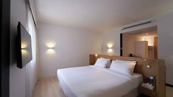 Habitación de hotel con una cama grande, mesitas de noche, un televisor de pantalla plana montado en la pared y dos lámparas de pared.