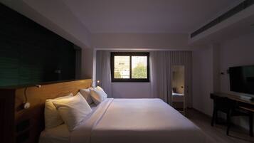 A hotel room with a large bed, a desk, a TV, and a window with curtains.