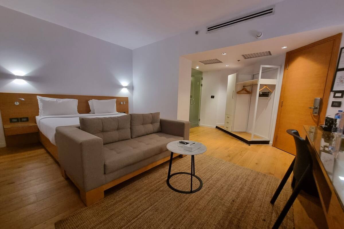 A modern hotel room with a bed, sofa, small table, and a walk-in closet.