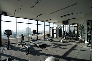Un gimnasio moderno con diversos equipos de ejercicio, amplias ventanas que ofrecen vistas de la ciudad y un diseño amplio y limpio.